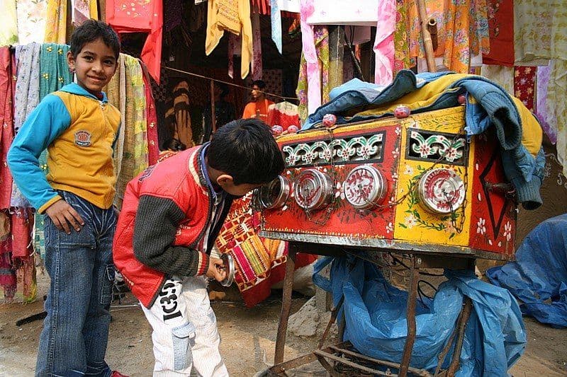 An Indian bioscope at a fair: several children watch at once through separate lenses while the showman narrates.