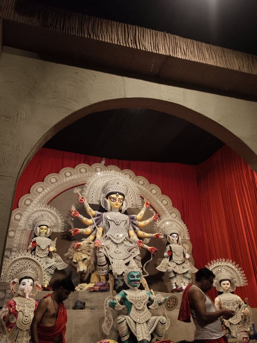 A Durga group at a Chittagong pandal dressed in white pith and silver foil, with matching filigree arches behind each figure.
