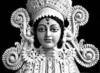 Close view of a Durga head crowned and framed in white filigree saj work, the ornament built up in cut relief.