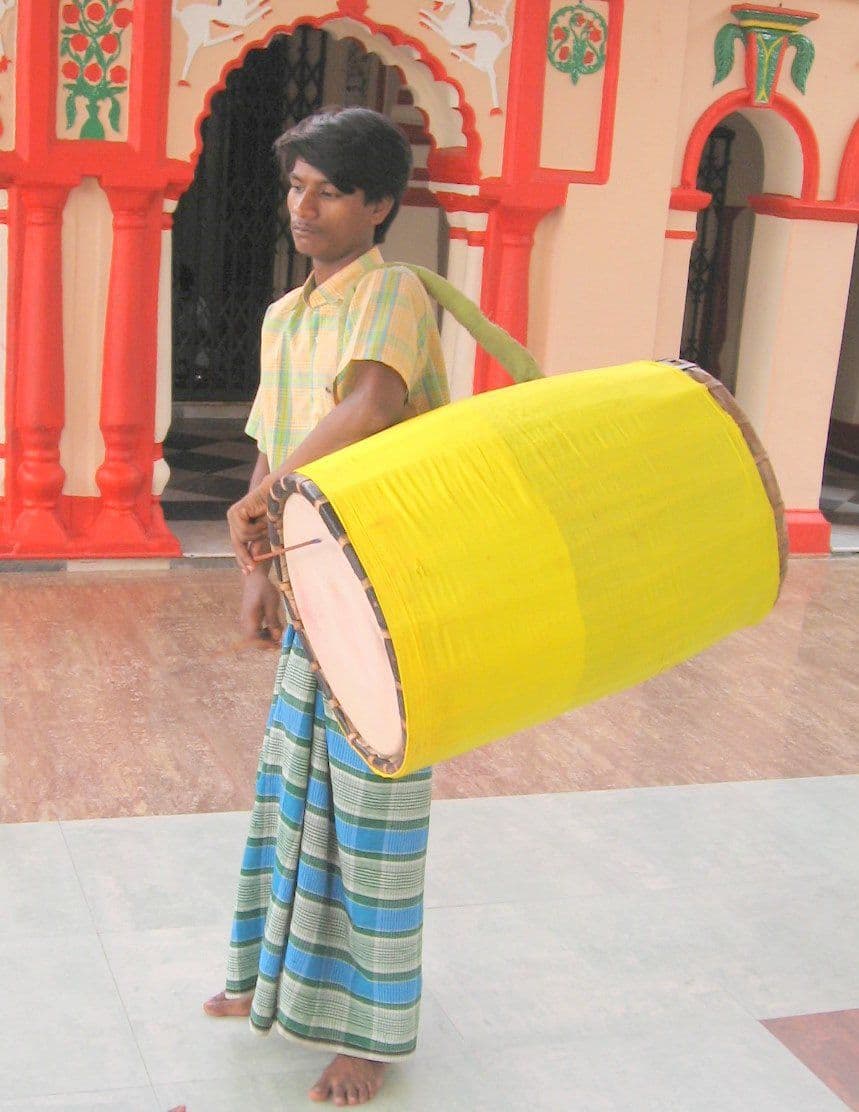 A young dhaki at Dhakeshwari temple, Dhaka, the yellow-wrapped barrel drum slung from one shoulder and struck with two cane sticks.
