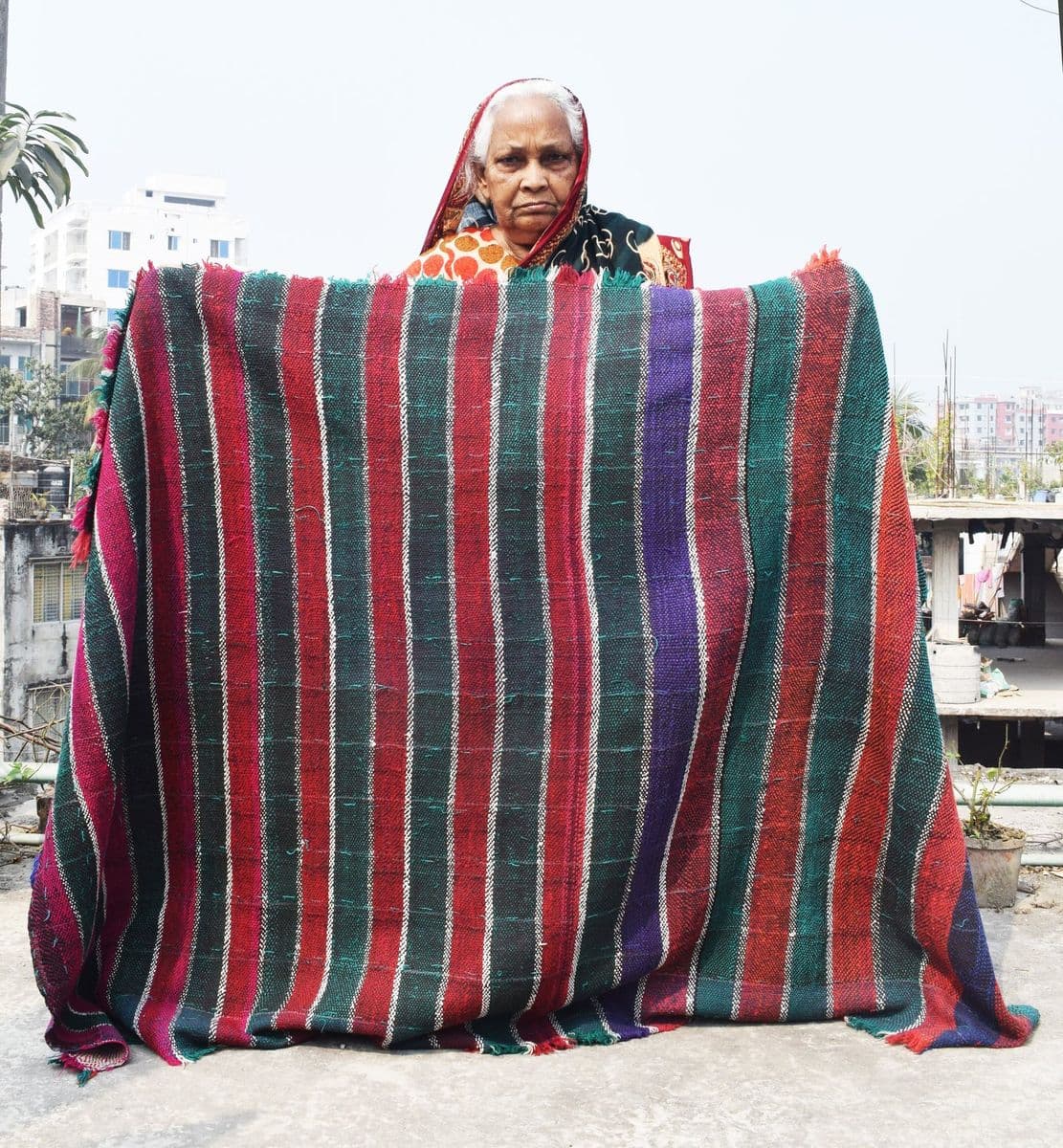 Shahera Khatun holding a large nakshi kantha she stitched, the scale at which a single household quilt is worked.