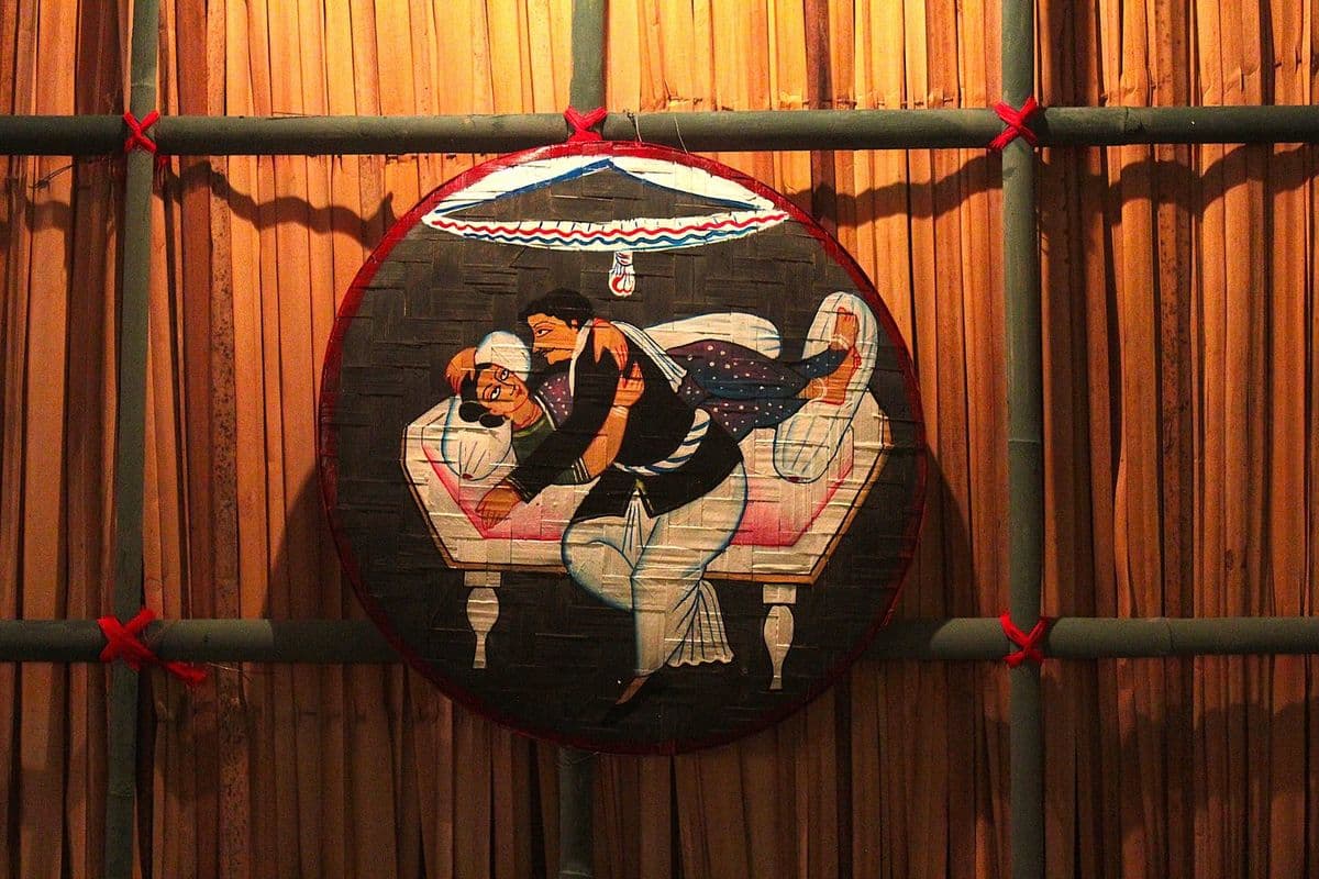 A pandal wall of split bamboo and reed matting carrying a painted Kalighat-style roundel, tied on with red cord.