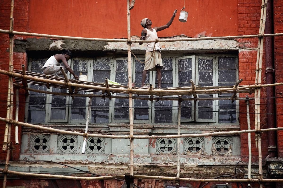 Two workers barefoot on a lashed bamboo scaffold in Kolkata, the same rope-tied joint used to build Durga Puja pandals.