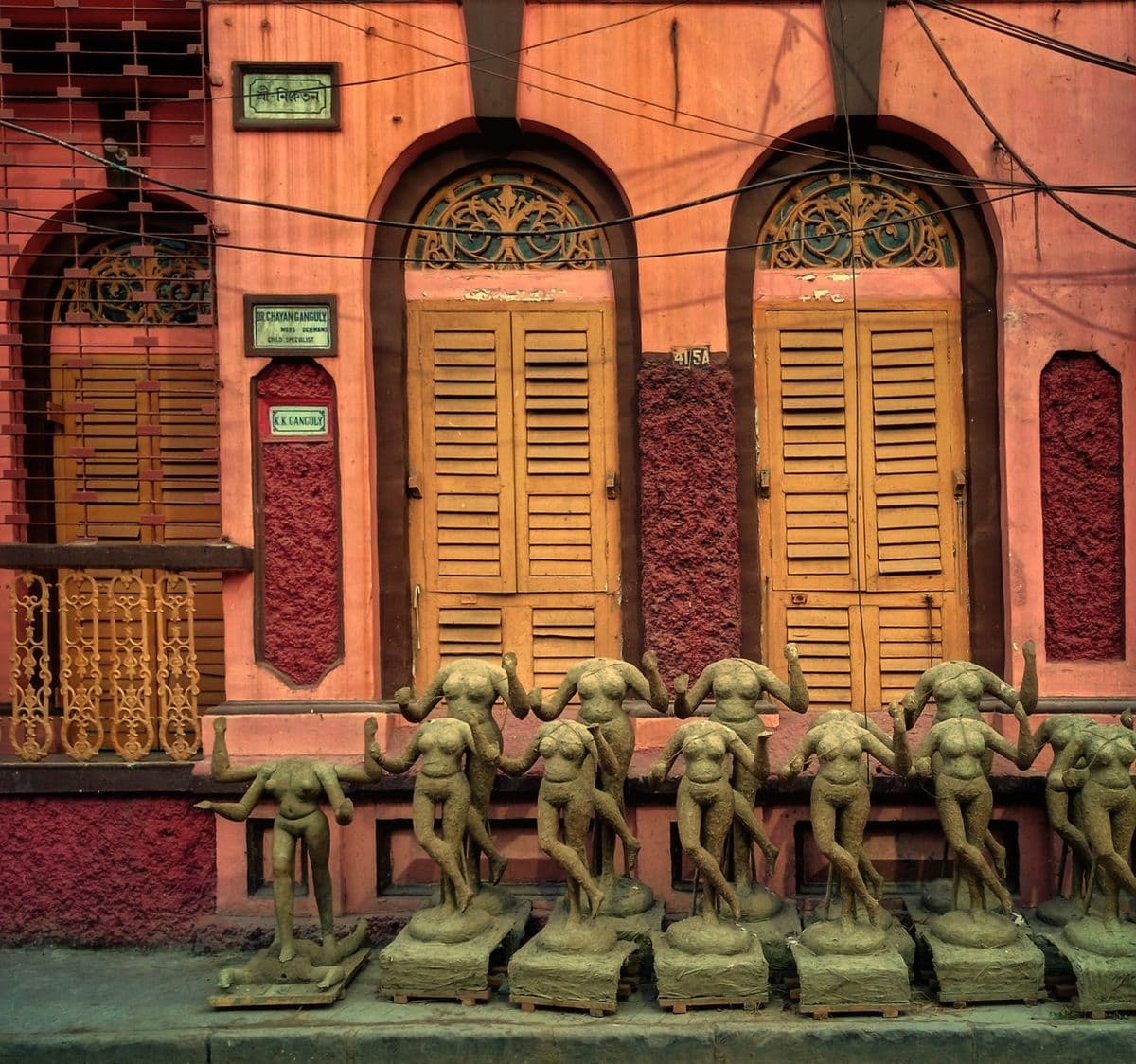 A row of unfinished Durga torsos in first-coat clay, drying on the pavement outside a shuttered Kumartuli house.