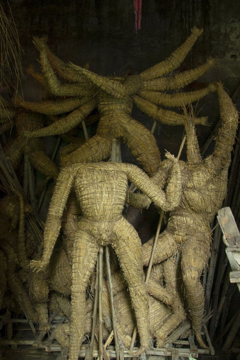 Straw armatures of Durga and her children stacked in a dark Kumartuli storeroom, waiting for their first coat of clay.