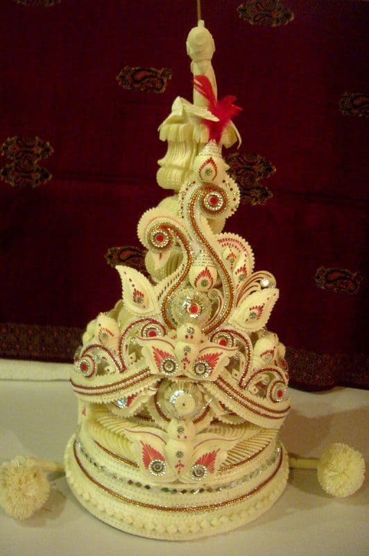 A Bengali groom's topor: conical shola headgear built from curled white pith ribbon and trimmed with red, gold and mirror.