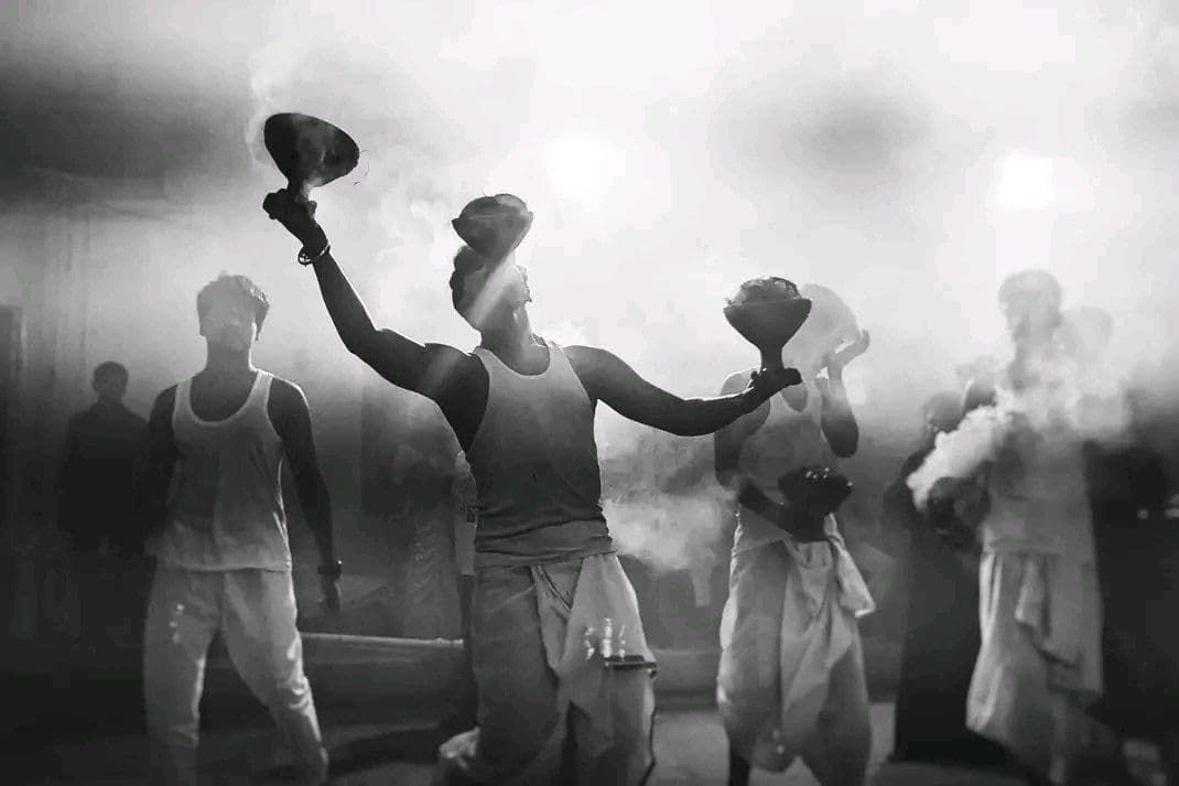 Four men in vests and dhotis swing earthen dhunuchis through thick smoke during evening arati at a Durga Puja.